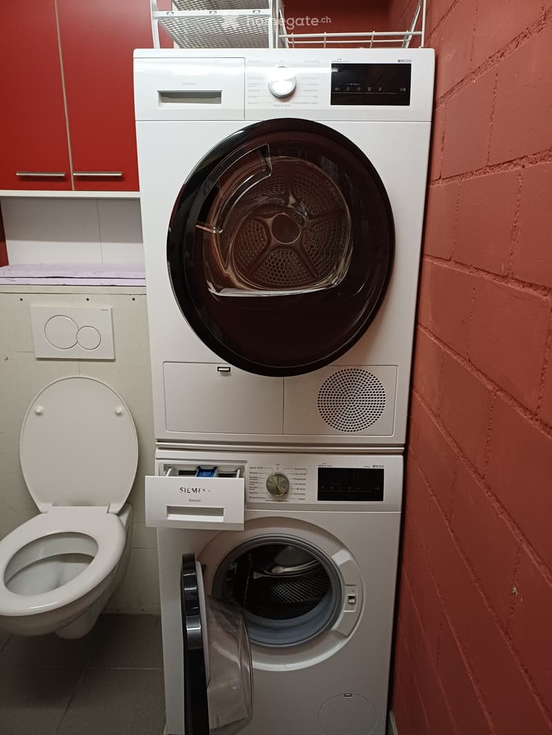 Bathroom with a stacked washing machine and dryer unit, a toilet, and red cabinets.