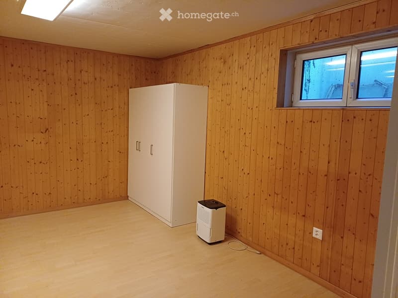 Empty room with wooden walls and floor, featuring a white cabinet and a small air conditioner unit near the window.