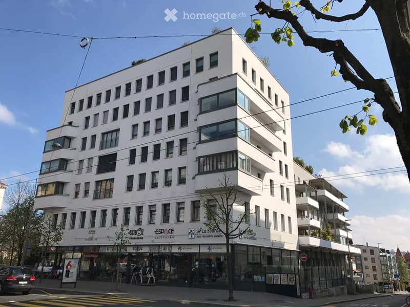 Modern apartment building with several floors, white exterior, multiple windows, rooftop balcony visible, commercial area at the ground floor.