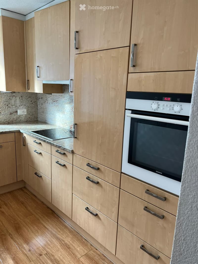 Modern kitchen with light wooden cabinets, stainless steel oven, granite countertop, and wooden flooring.