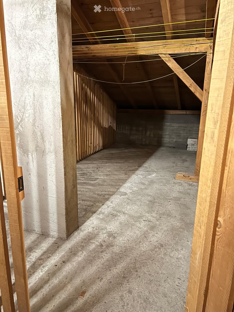 Empty unfinished hallway with exposed wooden beams, concrete floor, and electrical wires running along the ceiling.