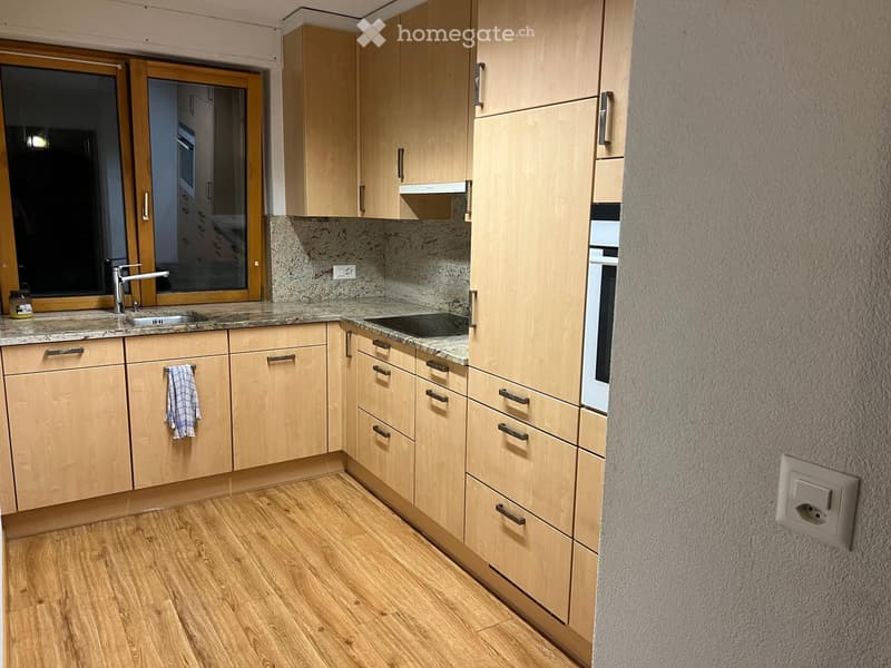 Modern kitchen with light wooden cabinets, granite countertops, and a stainless steel sink. Features include a built-in oven, a window, and a towel hanging from a cabinet door.