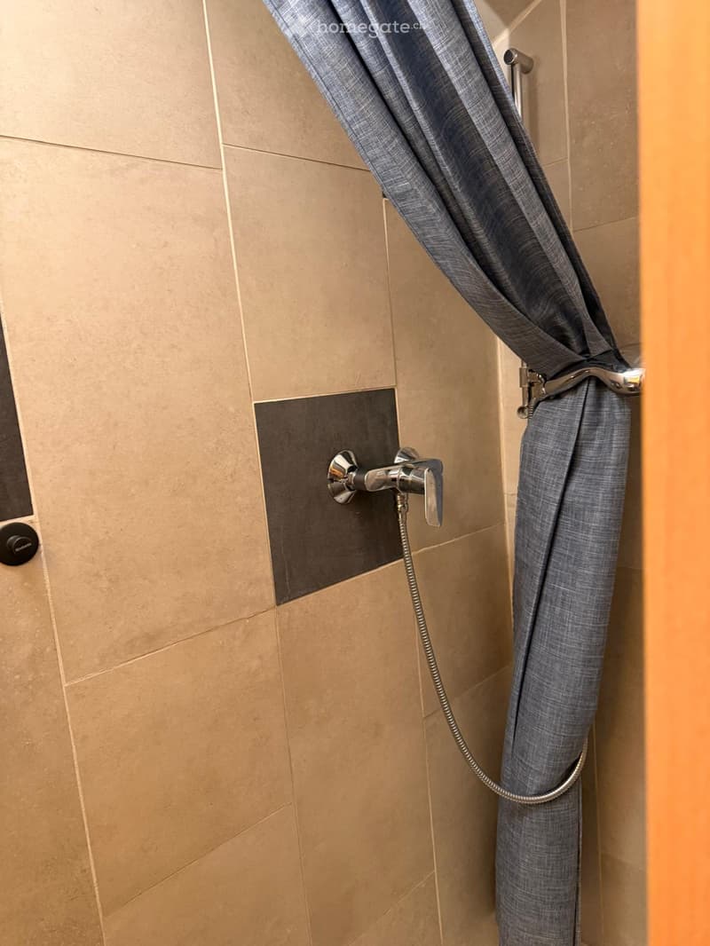 Modern shower area with beige tiles, a grey shower curtain, and a chrome faucet.