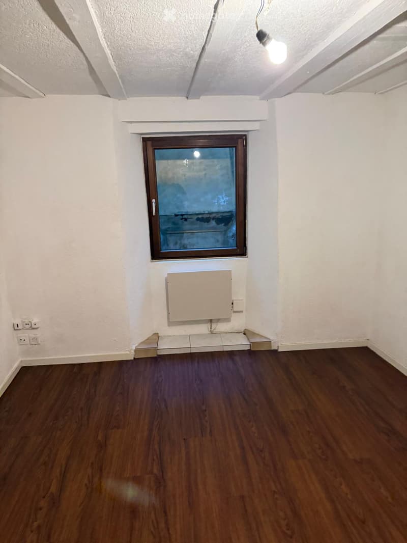 Empty room with wooden flooring, white walls, a single window, and a radiator. No furniture or equipment is present.