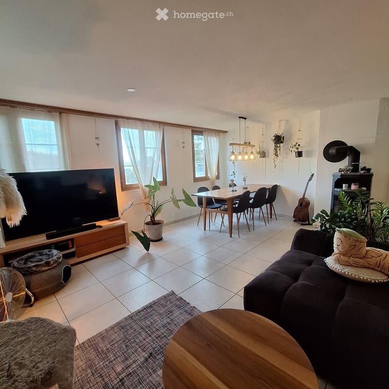 A modern living room with a large TV, a sofa, a coffee table, a dining area with a table and chairs, a guitar, and several plants. The room features large windows with curtains and a tiled floor.