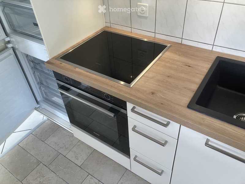 Modern kitchen with white cabinets, wooden countertops, induction stove, oven, and refrigerator.