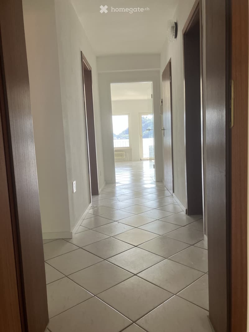 Empty hallway with tiled floor, white walls, and several doors leading to other rooms.