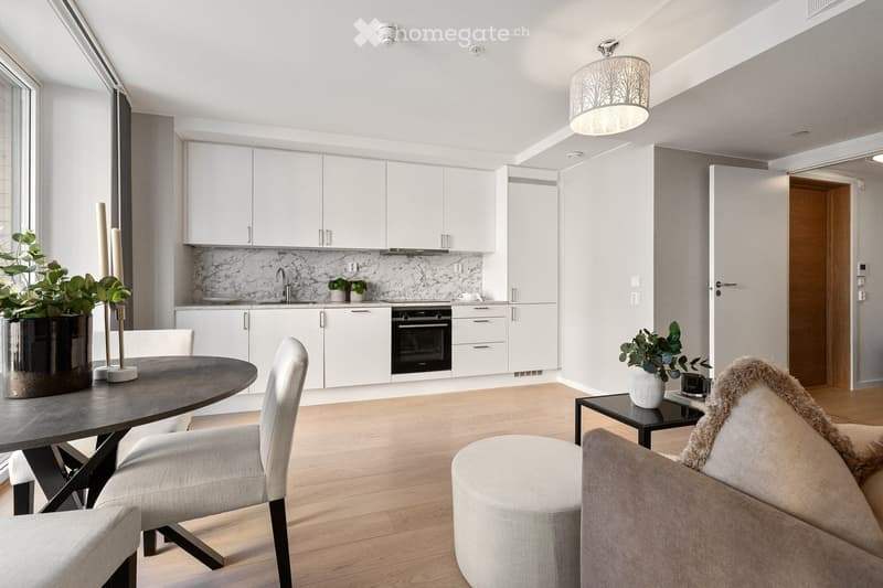 Modern open-plan living and dining area with a grey sofa, ottoman, coffee table, dining table, chairs, and a small kitchen with white cabinets, an oven, and a marble backsplash.