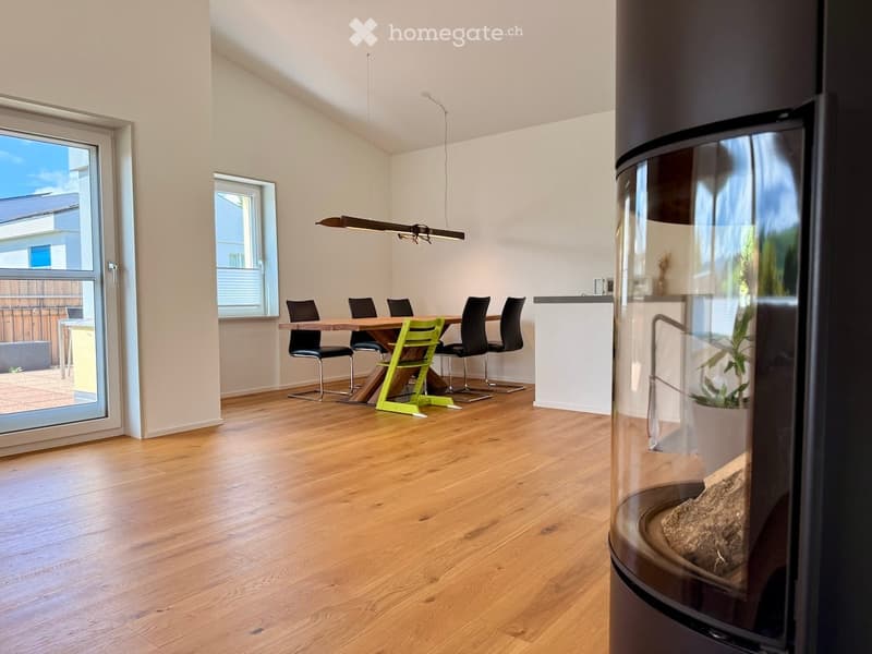 Bright dining area with wooden floor, modern fireplace, dining table with chairs, pendant light, and large windows with outdoor view.