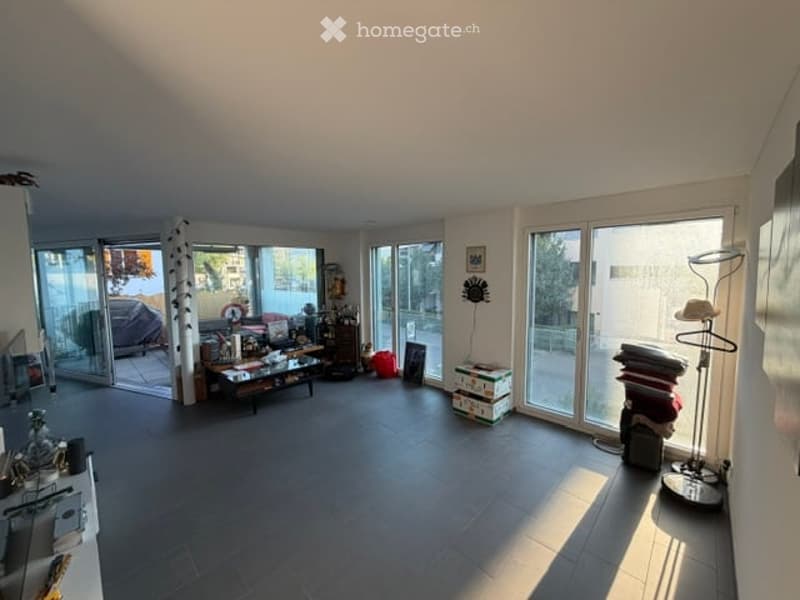 Bright living room with large glass doors leading to a balcony, featuring a coffee table, chairs, a mirror, a lamp, and storage boxes.