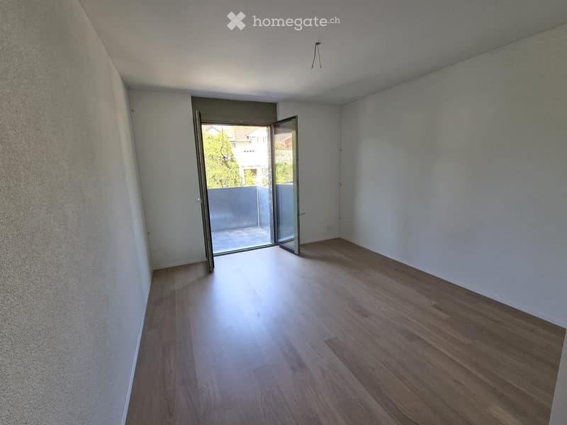 Empty room with light wooden flooring, white walls, and an open sliding door leading to a balcony area.
