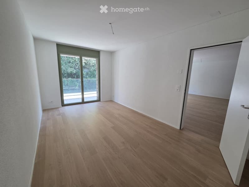 Empty room with light wooden flooring, white walls, and a sliding glass door leading to a balcony.