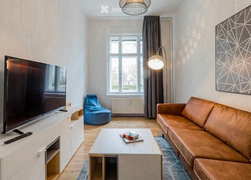 Modern living room with a brown leather sofa, coffee table, TV stand, bean bag chair, wall-mounted lamp, and wall art.