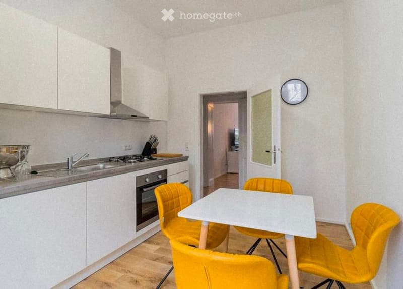 Modern kitchen with white cabinets, stainless steel appliances, and a small dining area with yellow chairs and a white table.