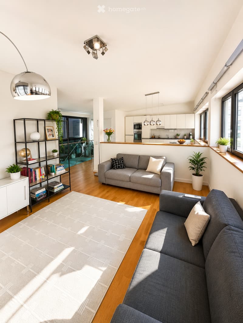 Modern living room with grey sofas, a coffee table, a bookshelf, and a kitchen area with white cabinets and stainless steel appliances.
