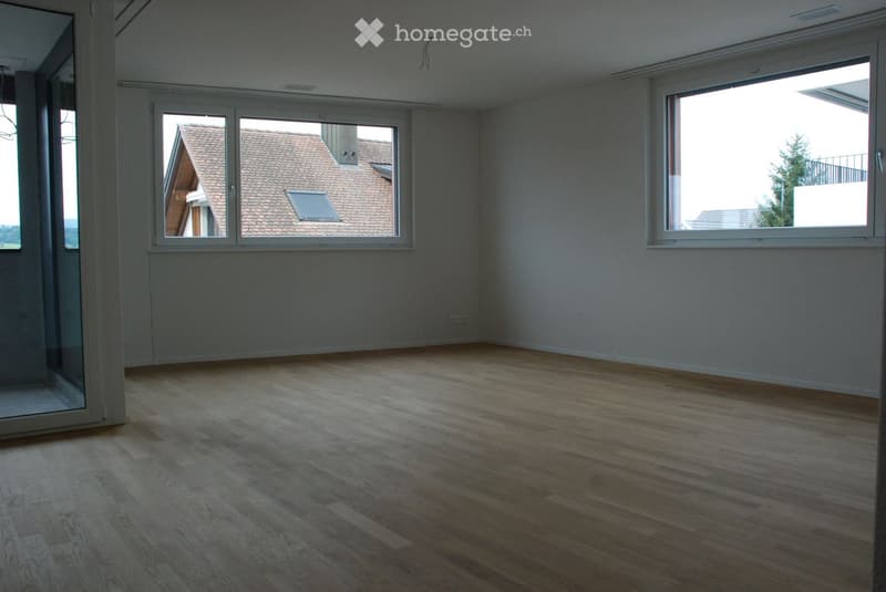 Empty room with wooden flooring, large windows, and white walls. No furniture or equipment present.