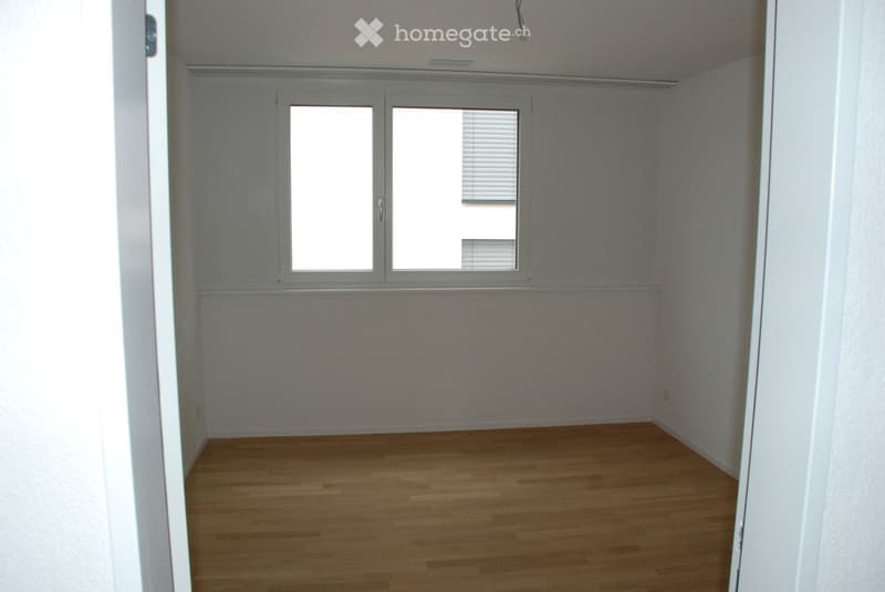 Empty room with wooden flooring, white walls, and large windows with blinds.