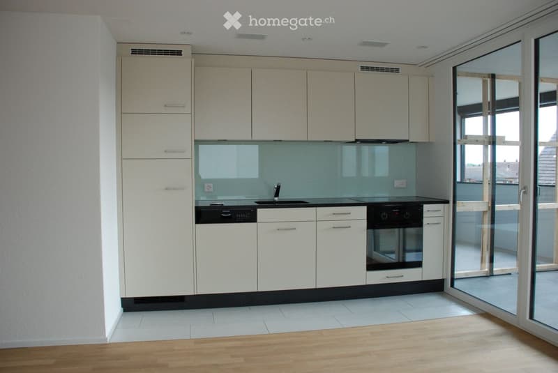 Modern kitchen with white cabinets, black countertops, and built-in appliances including a sink, faucet, oven, and dishwasher. Large glass sliding doors lead to a balcony.