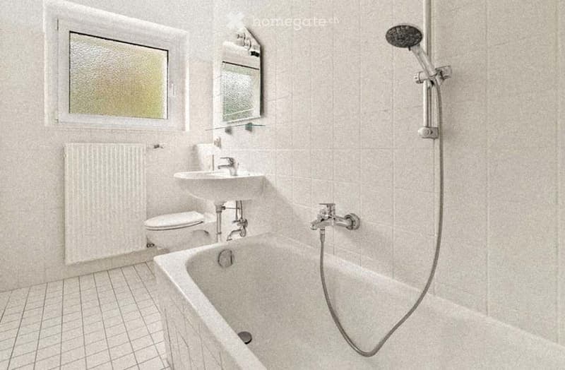 Bathroom with a bathtub, toilet, sink, mirror, and radiator. The walls and floor are tiled in a light color, and there is a window with frosted glass.