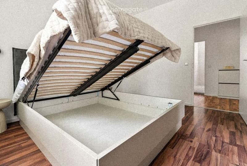 A modern bedroom with a raised platform bed and a nightstand visible in the background.