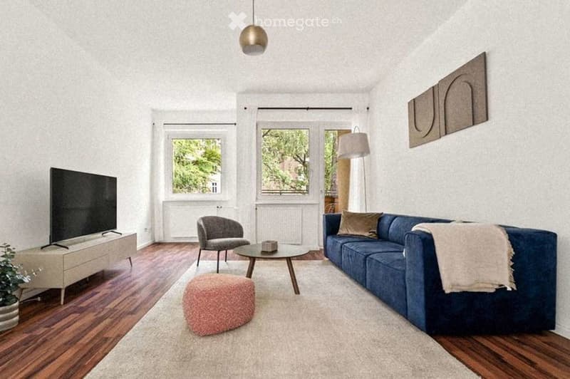 Modern living room with hardwood flooring, large windows, blue sofa, grey armchair, pink ottoman, coffee table, floor lamp, TV on side table, and decorative plant.