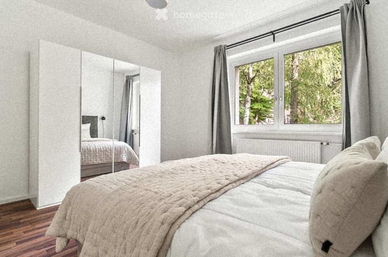 Cozy bedroom with a large bed, a mirrored wardrobe, and a window with curtains overlooking greenery.