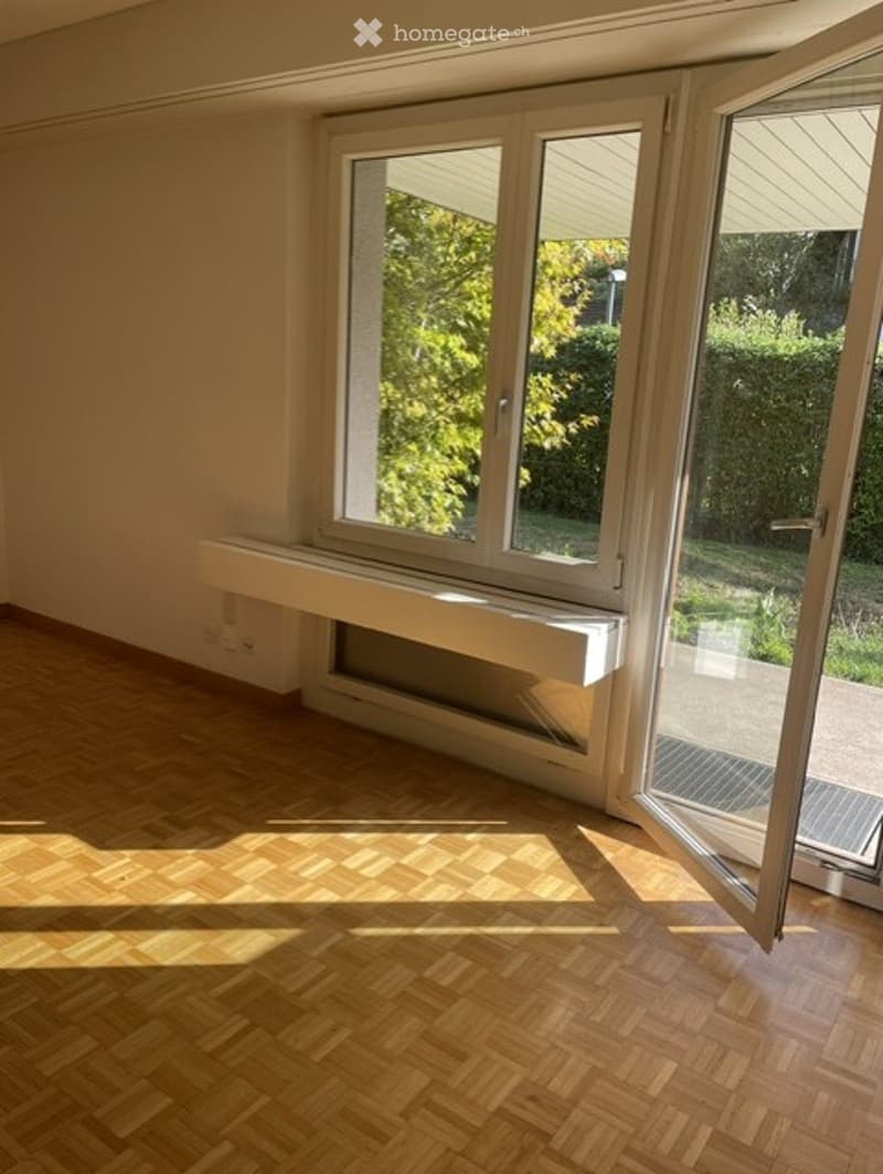 Empty room with wooden flooring, large window, and radiator below it. No furniture or equipment present.