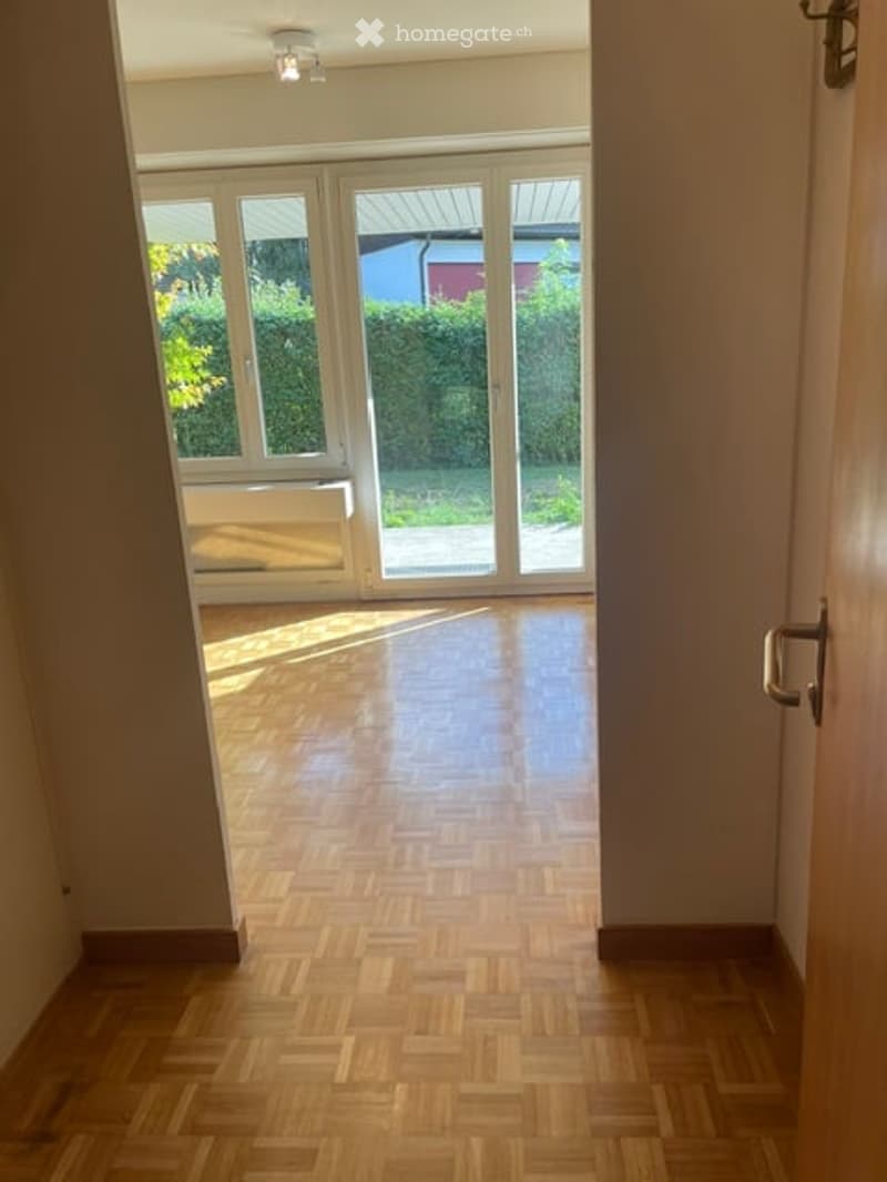 Empty room with wooden flooring and large glass doors leading to a garden area.