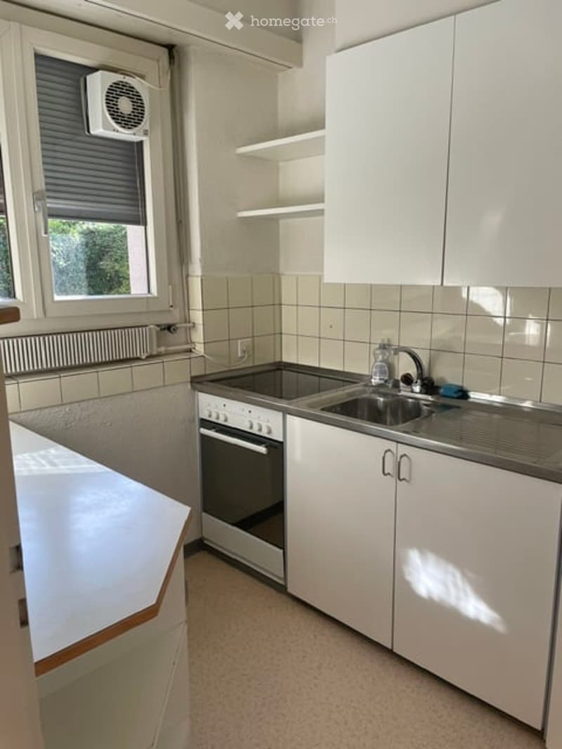 Modern kitchen with white cabinets, stainless steel sink, oven, and air conditioner above the window.
