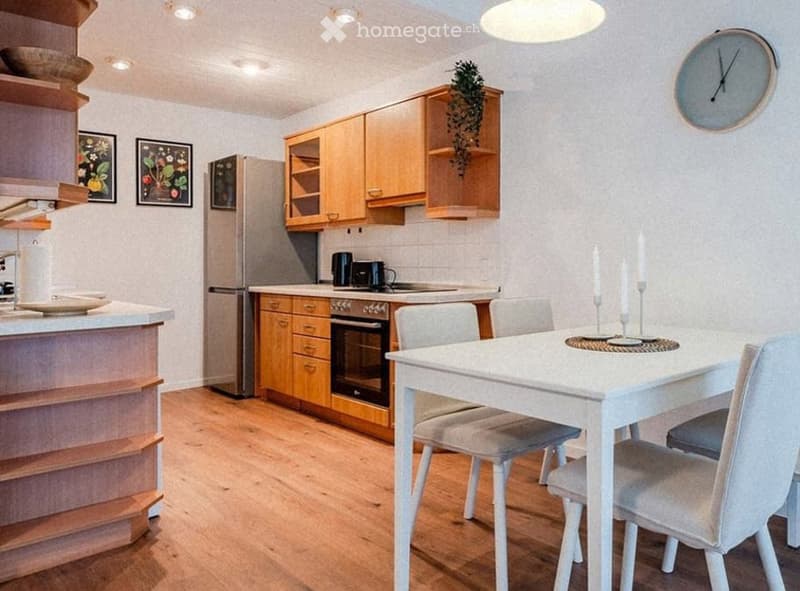 Bright kitchen with wooden cabinets, stainless steel appliances, a white dining table with four chairs, and a clock on the wall.