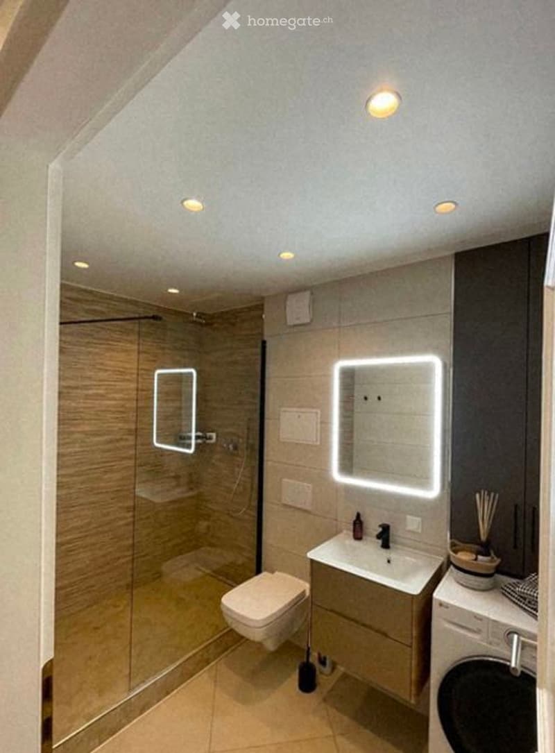 Modern bathroom with a glass-enclosed shower, a white toilet, a sink with a sleek faucet, and illuminated mirrors on the walls.