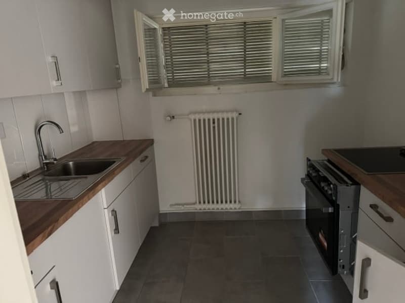 Modern kitchen with white cabinets, wooden countertops, stainless steel sink, and built-in oven. Features a radiator below a window with blinds.