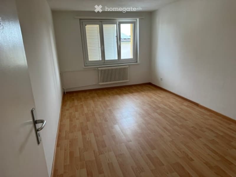 Empty room with wooden flooring, white walls, a window with blinds, and a radiator below the window.
