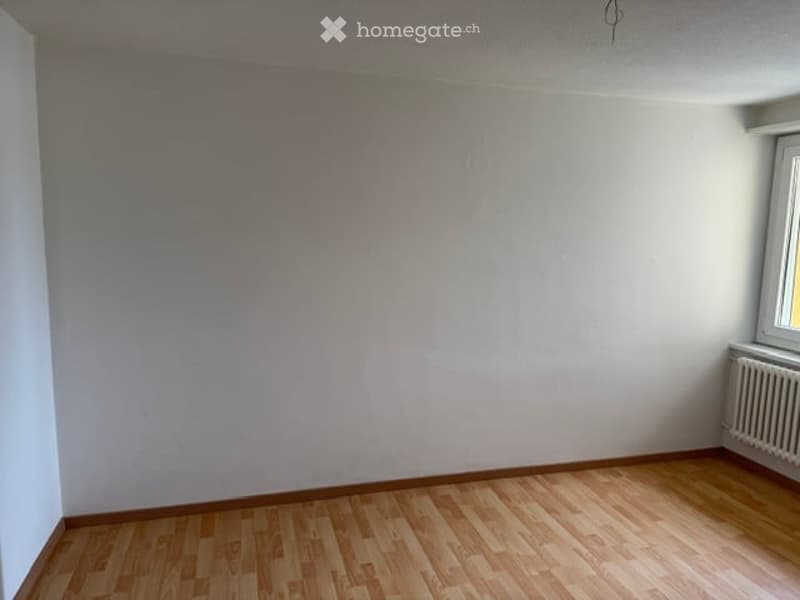 Empty room with wooden flooring and white walls, featuring a window and radiator on one side.