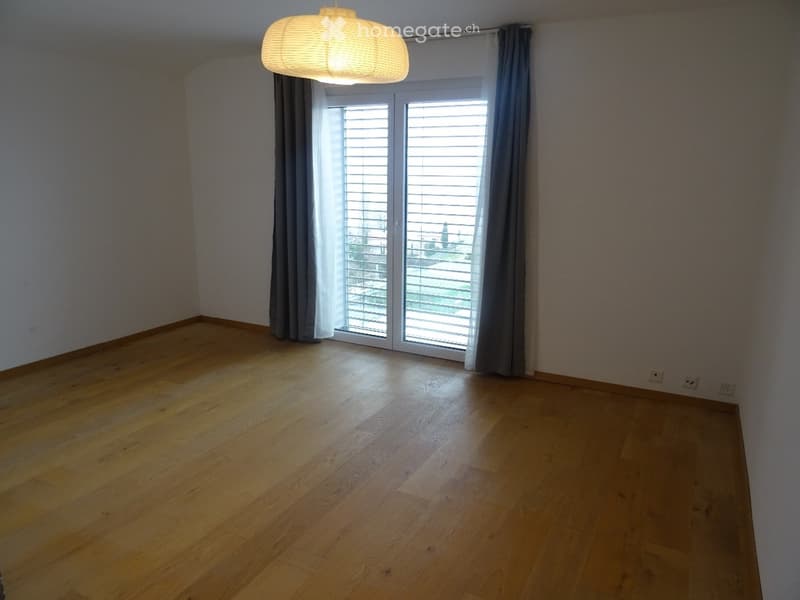 Empty room with wooden flooring, large window with blinds, and a hanging light fixture.