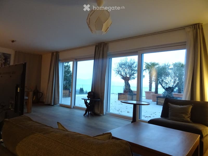 Modern living room with large sliding glass doors leading to a balcony, featuring a sofa, coffee table, and a small round table on the balcony.