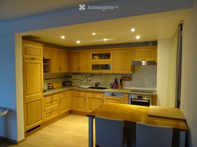 Bright kitchen with wooden cabinets, stainless steel appliances, a central island with a wooden countertop, and two chairs.
