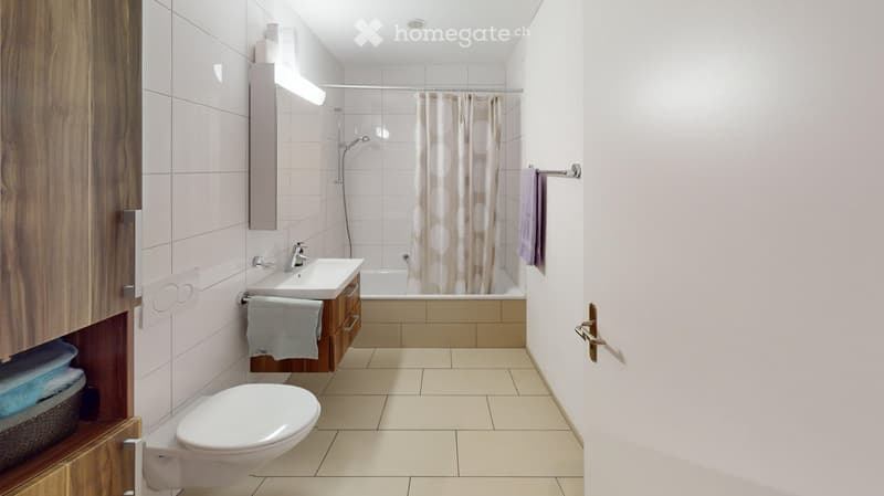 Modern bathroom with a toilet, sink, bathtub, and mirror. Features tiled walls and floor, wooden cabinetry, and a shower curtain.