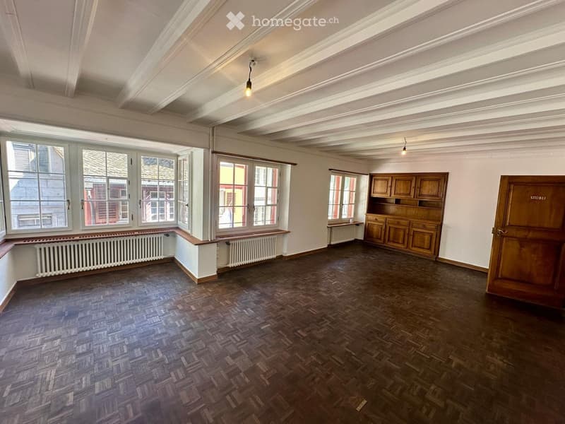 Empty room with wooden flooring, large windows, radiators, and built-in wooden cabinetry.