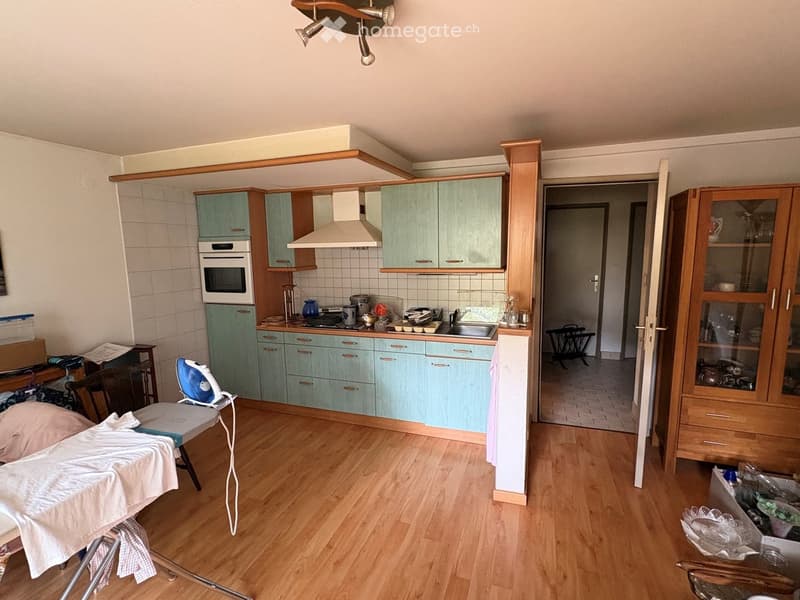 A well-equipped kitchen with light blue cabinets, a wooden floor, and various appliances including an oven, microwave, and refrigerator. An ironing board and iron are placed near the entrance.