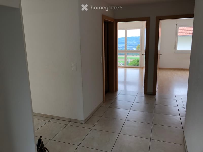 Empty hallway with tiled floor, white walls, and open doors leading to other rooms and a view of the outdoors.