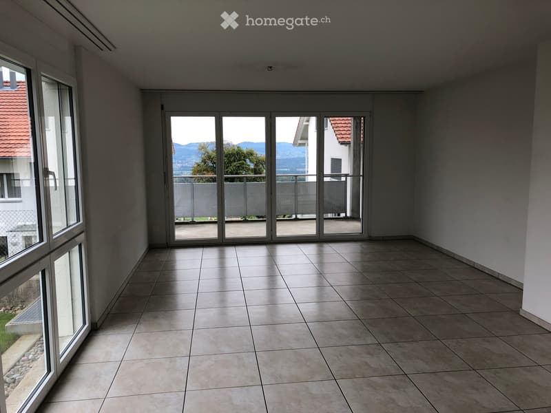 Empty room with tiled floor, large sliding glass doors leading to a balcony, and large windows on the left side.