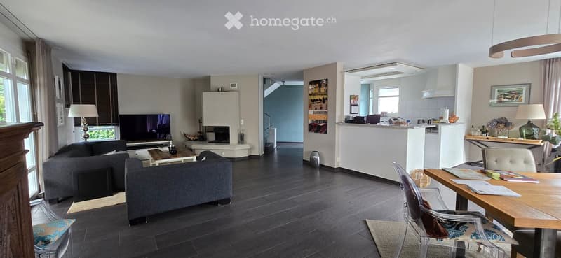 Modern living room with dark wooden flooring, grey sofa, coffee table, television, fireplace, and a small dining area with a table and chairs.
