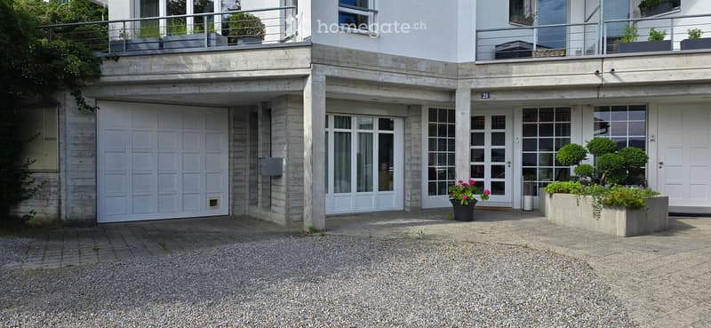 Modern two-story building with a large garage, white facade, large windows, and a balcony with planters.