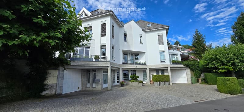 Modern two-story house with white exterior, multiple balconies, garage, and landscaped garden.