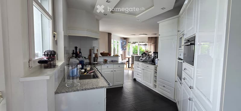 Modern kitchen with white cabinets, granite countertops, and stainless steel appliances. Features include a sink, microwave, oven, coffee machine, and various kitchen items on the counter.