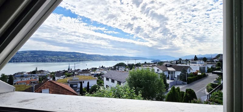 Balcony with scenic view of a town, lake, and distant mountains under a partly cloudy sky.