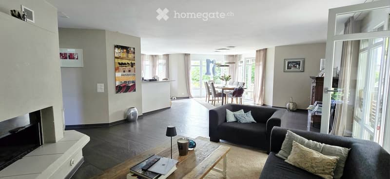 Modern living room with dark wooden flooring, a black sofa, a coffee table with a lamp, a fireplace, and a dining area with a table and chairs.