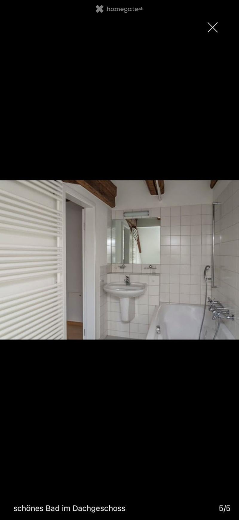 Bathroom with white tiled walls, a sink, a bathtub, and a mirror above the sink. Wooden beams are visible on the ceiling.
