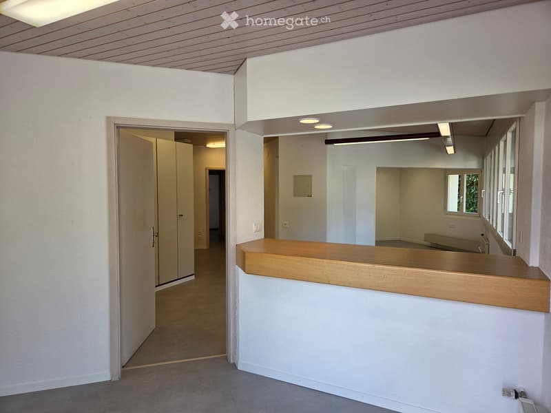 Empty room with white walls, wooden counter, open door, and windows